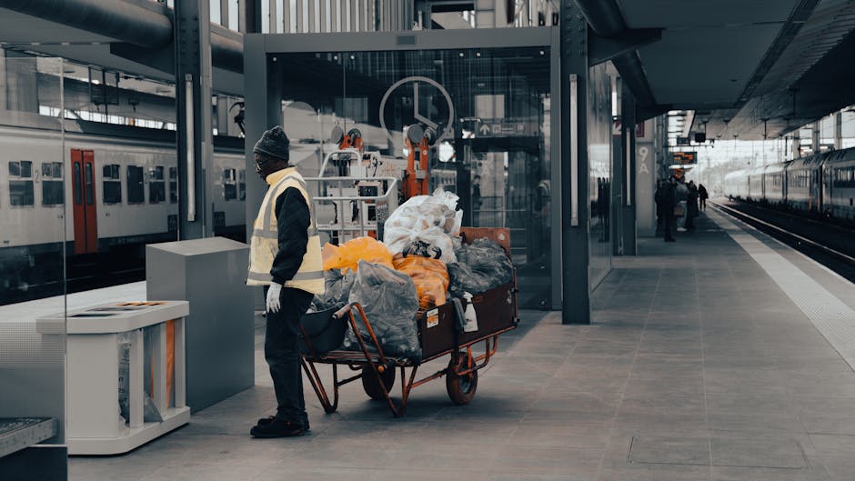 Inside a small, enclosed shelter with dark blue painted walls, a black plastic rubbish bin with yellow markings is positioned near the corner, standing on a concrete pavement. On the walls adjacent to